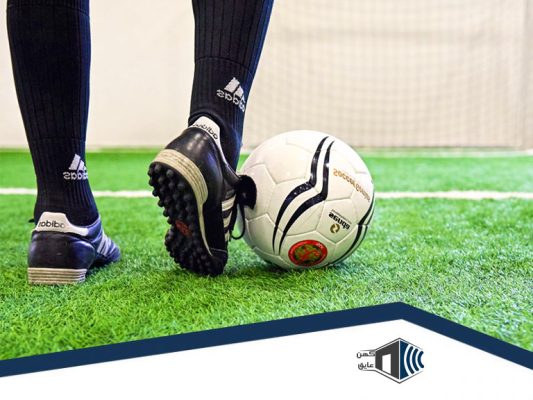 بازیکنان فوتبال در حال بازی روی چمن مصنوعی